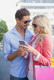 Stylish young couple looking at smartphone holding shopping bags