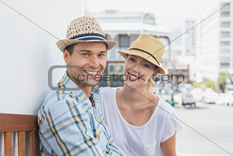 Young hip couple sitting on bench smiling at camera