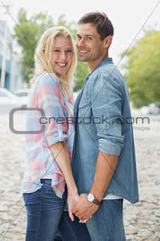 Hip young couple holding hands smiling at camera