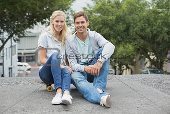Hip young couple sitting on skateboard smiling at camera