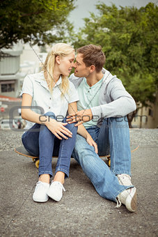 Hip young couple sitting on skateboard kissing