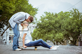 Hip young blonde sitting on skateboard with boyfriend kissing forehead
