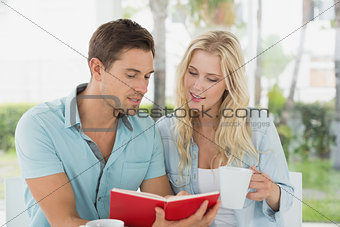 Hip young couple having coffee together reading book