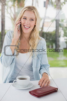 Pretty blonde sitting at table having coffee talking on phone