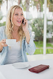 Pretty blonde sitting at table having coffee talking on phone