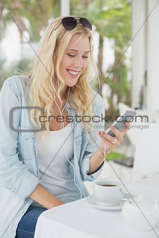 Pretty blonde sitting at table having coffee sending text