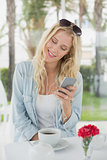 Pretty blonde sitting at table having coffee sending text