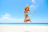 Woman with straw hat jumping mid-air at beach