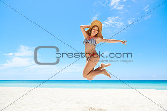 Woman with straw hat jumping mid-air at beach