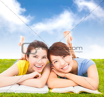 happy pretty students lying on the grassland with books