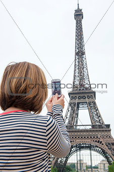 woman taking photographs of eiffel tower paris using a cellphone