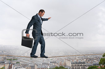 businessman walking tightrope above city