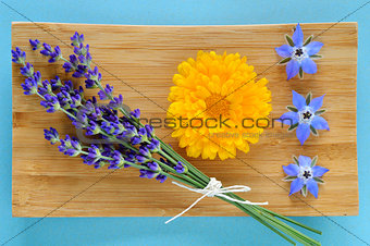 Summer herbs and edible flowers on wooden plate.