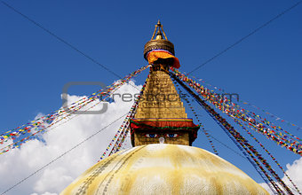 stupa with buddha eyes and prayer flags on clear blue sky