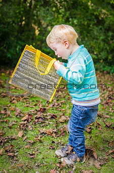 Cute surprised little blond boy looking inside bag outdoor