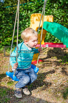 Cute little blond boy swinging on swings outdoor playground