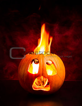 Scared face of Halloween pumpkin with flames and red smoke in the background.