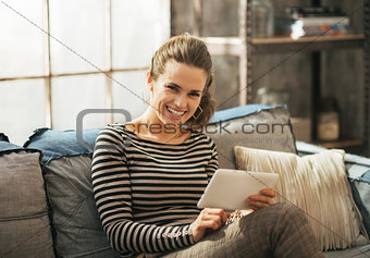 Smiling young woman sitting on sofa and using tablet pc in loft 