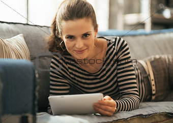 Young woman laying on couch and using tablet pc in loft apartmen