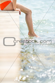 Closeup on young woman sitting on bridge with legs in water