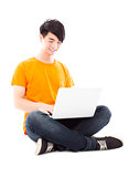 Smiling young student sitting on floor and  using laptop