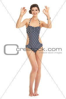 Full length portrait of smiling young woman in swimsuit showing 