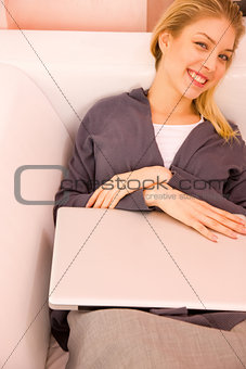 Smiling young woman with laptop lying couch