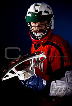 Lacrosse player wearing helmet and holding stick. Studio shoot on the black background with blue light spot.