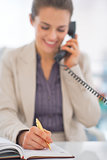Closeup on business woman talking phone and writing in diary