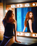 Portrait of beautiful young red-haired woman looking into mirror
