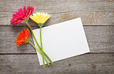 Three colorful gerbera flowers and blank greeting card
