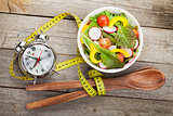 Fresh healthy salad and measuring tape on wooden table