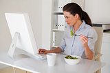 Casual brunette businesswoman eating a salad at her desk