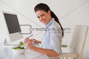 Casual brunette businesswoman eating a salad at her desk