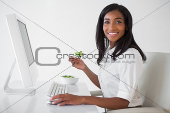 Casual pretty businesswoman eating a salad at her desk