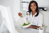 Smiling businesswoman eating a salad at her desk