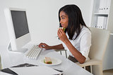 Smiling businesswoman having a sandwich at her desk