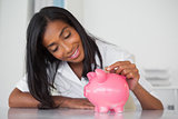 Smiling businesswoman putting coins into piggy bank at her desk