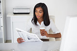 Pretty businesswoman reading newspaper at her desk