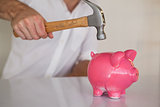 Casual businessman breaking piggy bank with hammer