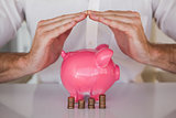Casual businessman sheltering piggy bank and coins