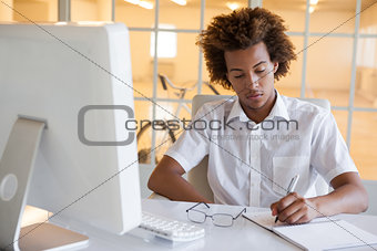 Casual young businessman writing at his desk