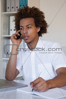 Focused casual businessman on the phone taking notes at desk