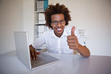 Casual businessman smiling at camera at his desk showing thumbs up