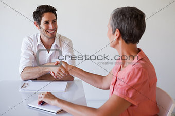 Casual business people shaking hands at desk and smiling