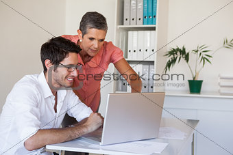 Casual business team working together at desk using laptop