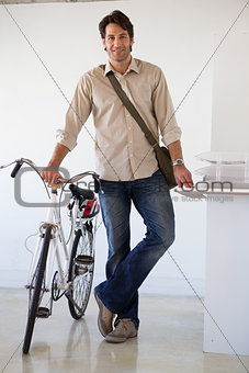 Casual businessman standing with his bike smiling at camera