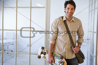 Casual businessman standing with his skateboard smiling at camera