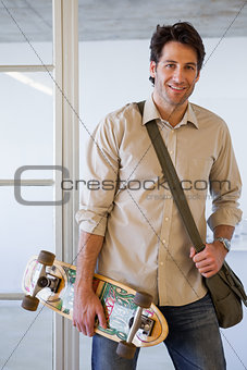 Casual businessman standing with his skateboard smiling at camera
