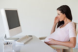 Casual pregnant businesswoman thinking at her desk